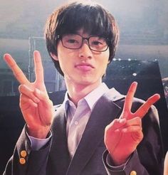 a young man in glasses making the peace sign with his fingers while wearing a suit and tie