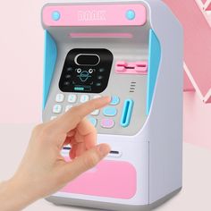 a child's hand is pressing the button on a toy atm machine that appears to be pink and blue