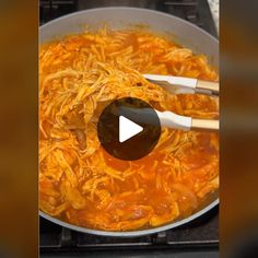 a pan filled with noodles and carrots on top of an electric stove, being stirred by two wooden spoons