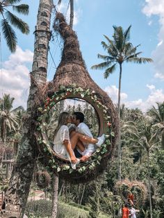 a man and woman are kissing in a circular mirror surrounded by palm trees on the beach