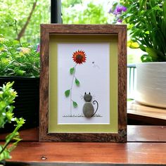 a cat sitting next to a flower in a wooden frame