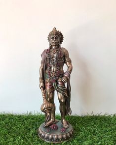 a statue of a man holding a ball in his hand on some green grass with a white wall behind it