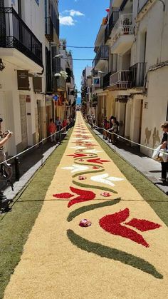 people are walking down an empty street lined with flowers