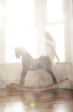 a woman riding on the back of a wooden rocking horse in front of a window