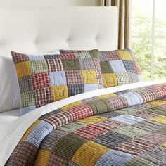 a bed with a white headboard and colorful quilts on the comforter in front of a window