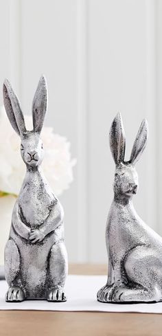 two silver rabbit figurines sitting on top of a table next to a vase with flowers