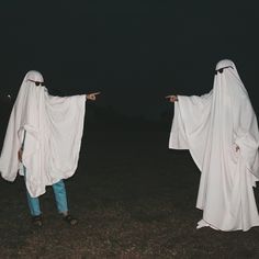 two people dressed in ghost costumes pointing at something