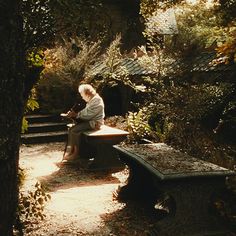 an old woman sitting on a bench in the woods