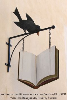 an open book hanging from the side of a building with a bird on it's back