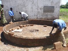 two men are building a brick wall around a circle in the middle of a dirt field