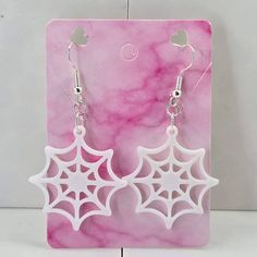 white spider web earrings on pink marble background