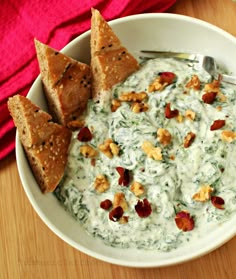 a white bowl filled with spinach and crackers on top of a wooden table