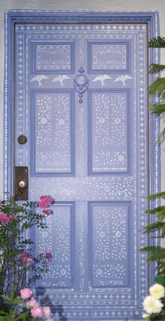 a blue door with white designs on it and some flowers in front of the door