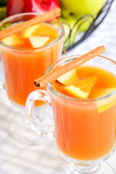 two mugs filled with orange juice and cinnamon stick garnished with apple slices