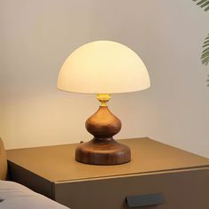 a table lamp sitting on top of a wooden dresser next to a bed with white sheets