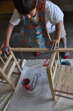 a little boy that is standing in front of a wooden chair with paint on it