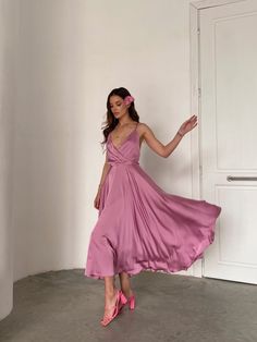 a woman in a pink dress standing next to a white door with her hand on her hip