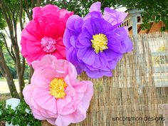 three large paper flowers sitting on top of a wooden table next to a bush and tree