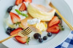 a white plate topped with pancakes, berries and whipped cream next to a fork on a blue checkered table cloth