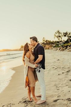 a man and woman kissing on the beach at sunset with palm trees in the background