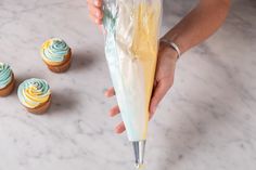 a person holding an umbrella over cupcakes on a marble table with frosting