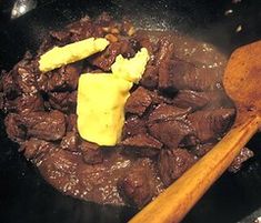 beef and potatoes cooking in a skillet with a wooden spoon