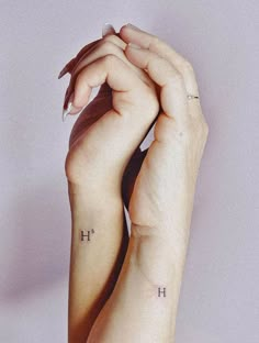 two hands holding each other with small tattoos on their wrist and the word h written across them