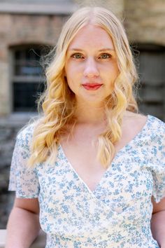 a woman with blonde hair wearing a blue and white floral dress standing in front of a brick building