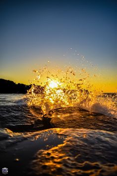 the sun is setting over the ocean as waves crash in front of an orange and blue sky