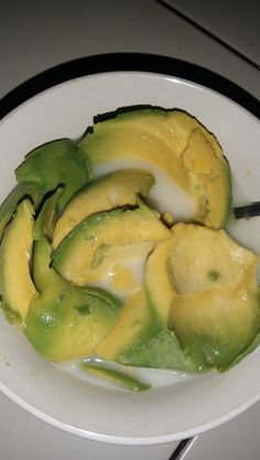 a white plate topped with sliced avocado on top of a counter next to a knife