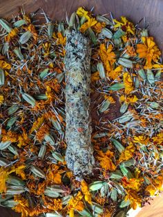 an assortment of dried flowers and herbs arranged on a wooden platter with a stick in the center