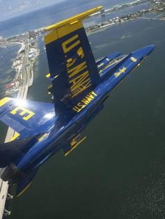 a blue and yellow jet flying over the ocean next to an airport in the sky