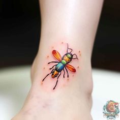 a small tattoo on the foot of a woman's leg with a colorful bee