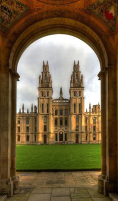 an archway leading to a large building with a clock on it's side and grass in the foreground