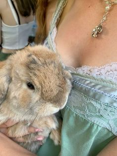 a woman is holding a small rabbit in her arms while wearing a green dress and necklace