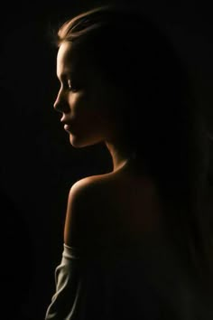 a woman standing in the dark with her hair blowing back and looking off to the side