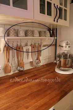 a wooden counter top in a kitchen with white cabinets and utensils hanging on the wall