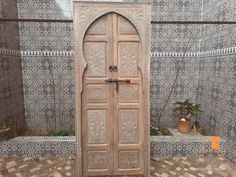 an old wooden door in front of a tiled wall with potted plants on it