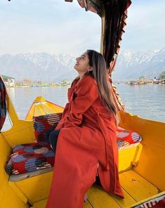 a woman sitting on the back of a yellow boat looking up into the sky with mountains in the background