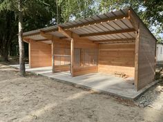 an outdoor shelter with wooden walls and doors on the outside, in front of some trees