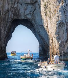 two boats in the water near a large rock formation with an arch on it's side