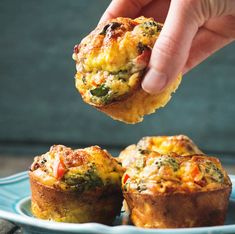 a hand holding a muffin over a blue plate with other muffins on it