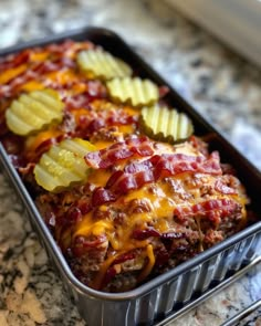 a metal container filled with meat covered in cheese and pickled up potato wedges