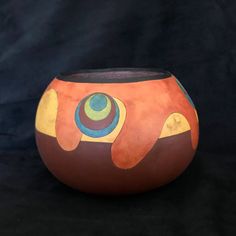 an orange and yellow vase with circles painted on the side, sitting on a black background