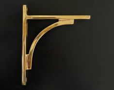 a gold metal shelf bracket on a black surface with the corner cut out to show it's shape