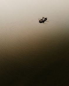 two people in a small boat floating on top of a body of water with fog