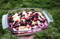 a person holding up a dish with berries and cream in it