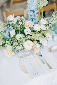 the table is set with blue and white flowers, silverware, and menu cards