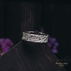 a wedding ring sitting on top of a piece of wood next to purple flower petals