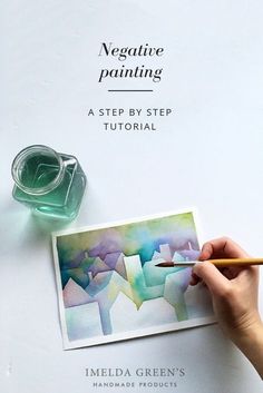 a person is holding a pencil and drawing on paper with watercolors in front of them